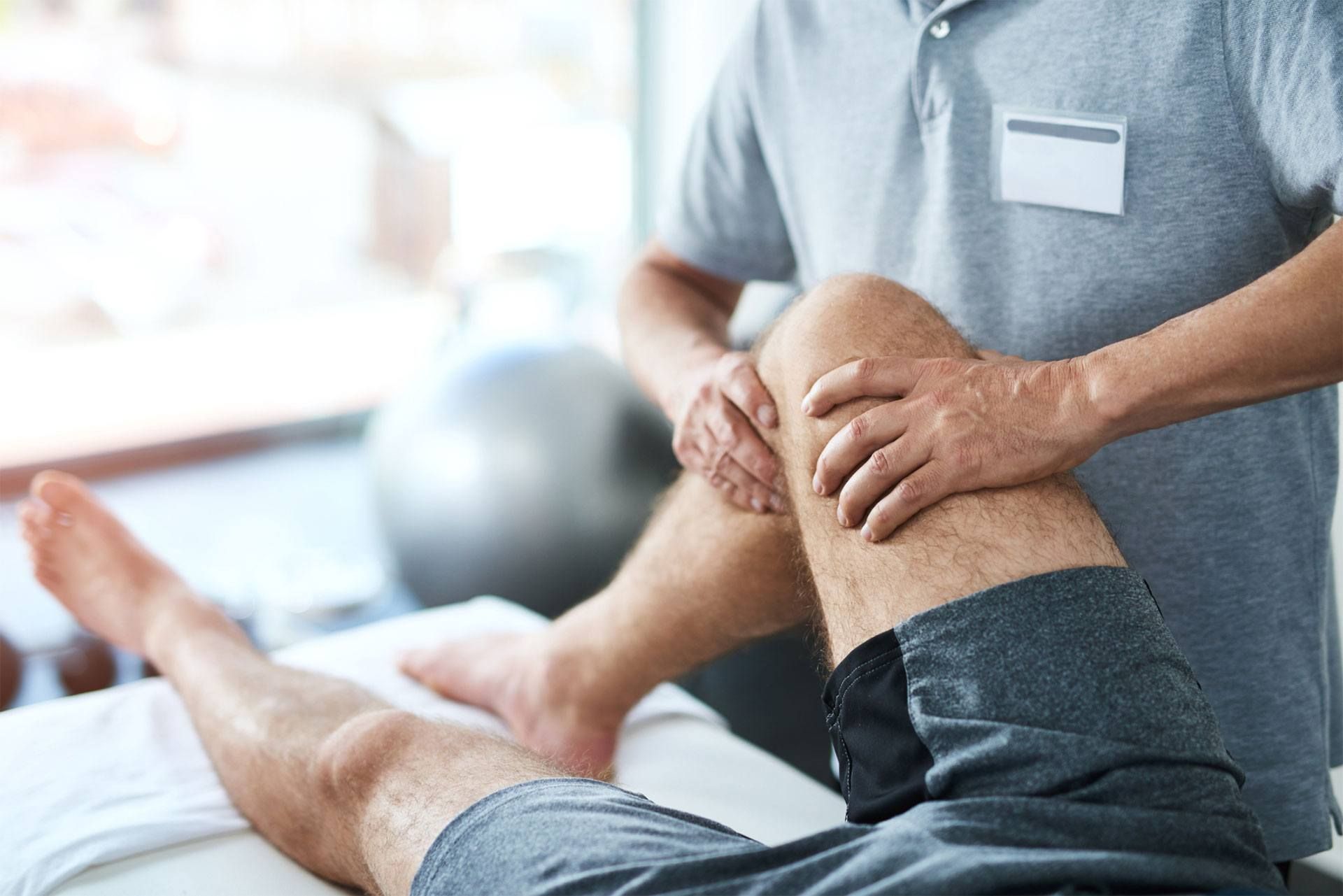 Physiotherapeut behandelt das Knie eines Patienten auf der Therapieliege